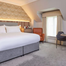 Deluxe room with king bed, elegant decor, cosy armchair, natural light, perfect for a relaxing stay with modern amenities.