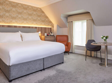 Deluxe room with king bed, elegant decor, cosy armchair, natural light, perfect for a relaxing stay with modern amenities.