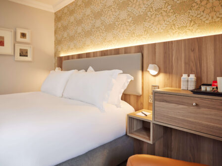 Cosy hotel room with plush bedding, warm lighting, stylish wallpaper, and amenities like bottled water and tea set.