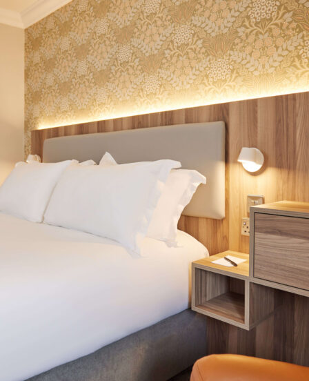 Cosy hotel room with plush bedding, warm lighting, stylish wallpaper, and amenities like bottled water and tea set.