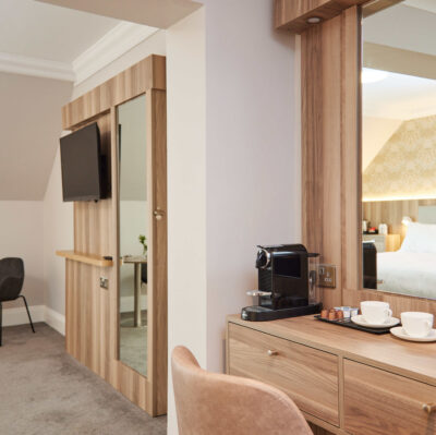 Cosy hotel room with stylish furnishings, a coffee machine, comfy bed, and flat-screen TV, perfect for relaxation.