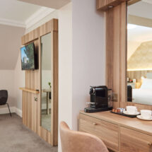 Elegant hotel room with plush bed, cosy seating area, large TV, and coffee station; perfect for a relaxing stay.