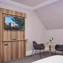 Elegant hotel room with twin beds, wall-mounted TV, cosy seating area, and soft lighting, offering comfort and relaxation.