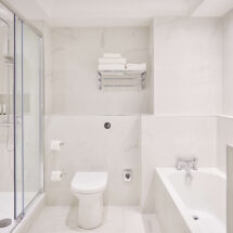 Elegant white marble bathroom with walk-in shower and bathtub, plush towels, and modern fixtures at luxury city hotel.