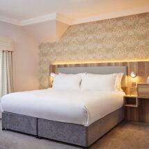 Elegant hotel room with plush king-size bed, soft lighting, stylish wallpaper, and convenient bedside amenities.