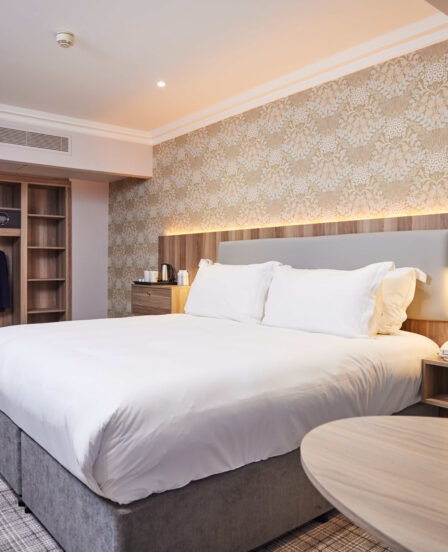 Spacious hotel room with king-size bed, elegant floral wallpaper, desk area, and wardrobe. Relaxing and luxurious stay.
