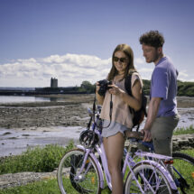 Guests enjoy cycling by the scenic seaside with castle views; perfect for outdoor adventures at our coastal hotel retreat.
