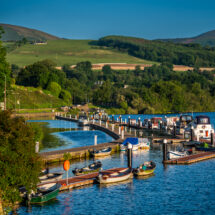 Charming lakeside view with boats and lush green hills at peaceful countryside hotel marina.