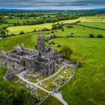 Aerial view of ancient stone abbey surrounded by lush green fields, capturing peaceful Irish countryside experience.
