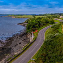 Coastal road with scenic sea views, lush greenery, and charming cottages, ideal for a relaxing countryside getaway.