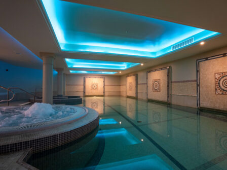 Luxurious indoor hotel pool with mosaic walls, soft glowing lights, and inviting jacuzzi, perfect for relaxation.