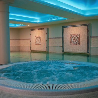 Luxurious hotel indoor spa pool with warm lighting, mosaic tiles, and a soothing jacuzzi for relaxation.