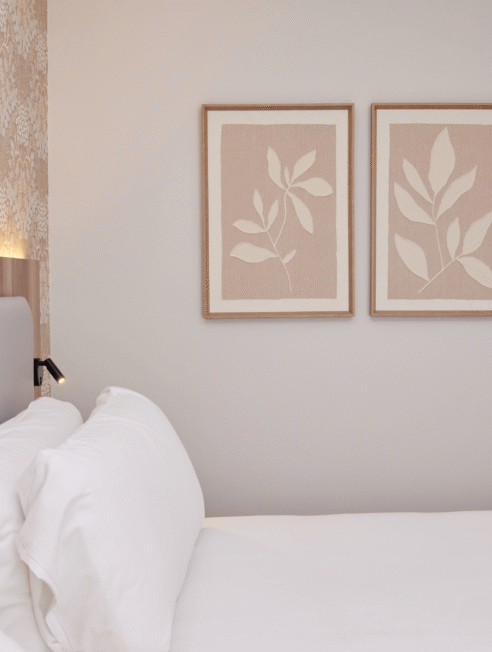 Elegant hotel room with plush white bedding, botanical art, soft lighting, and stylish wallpaper for a relaxing stay.
