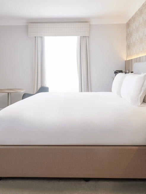 Spacious hotel room with king-sized bed, modern decor, flat-screen TV, and large window for natural light.