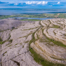 Stunning aerial view of rugged limestone landscape with lush fields and distant coastline under a blue sky.