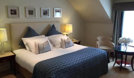 Cosy hotel room with king-size bed, elegant blue bedding, soft lighting, art on walls, perfect for a relaxing stay.