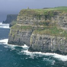 Stunning coastal cliffs with lush green tops, crashing blue waves below; perfect for a serene and scenic hotel retreat.