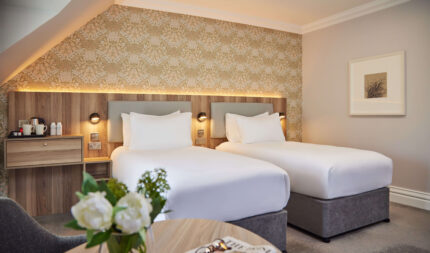 Executive twin room featuring two single beds, smart 43-inch TV, high-speed Wi-Fi, air conditioning, Nespresso station, and modern bathroom with rainfall shower