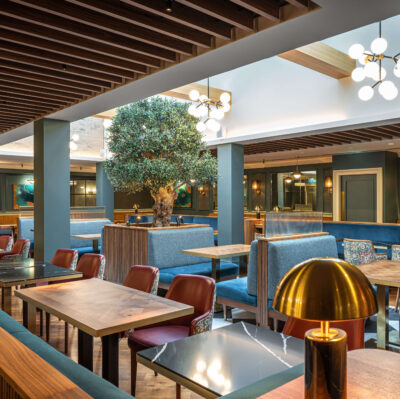 Elegant hotel dining area with warm lighting, modern wooden decor, plush blue seating, and inviting ambience.