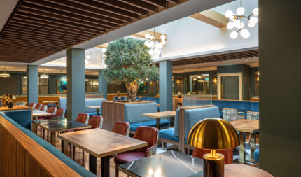 Elegant hotel dining area with warm lighting, modern wooden decor, plush blue seating, and inviting ambience.