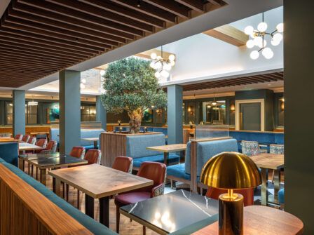 Elegant hotel dining area with warm lighting, modern wooden decor, plush blue seating, and inviting ambience.