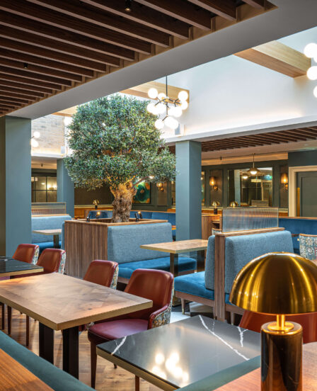 Elegant hotel dining area with warm lighting, modern wooden decor, plush blue seating, and inviting ambience.