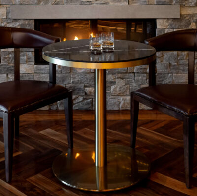 Elegant hotel lounge with cosy fireplace, round table, leather chairs, and ambient lighting.