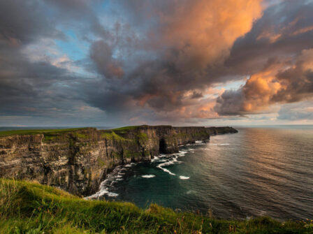 Stunning view of dramatic cliffs at sunset over the ocean, with lush green grass, perfect for a coastal retreat.