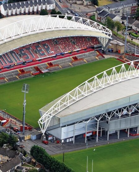 Aerial view of Huddersfield stadium with lush green pitch, surrounded by modern stands and nearby residential area.