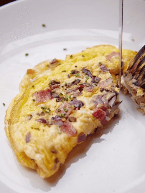 Enjoy a gourmet omelette with fresh herbs and diced ham in our hotel dining room, offering a delightful breakfast experience.