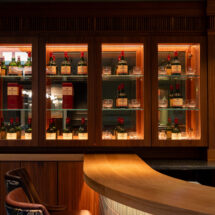 Elegant hotel bar with a warm wooden counter, stocked with premium spirits, inviting seating, and ambient lighting.
