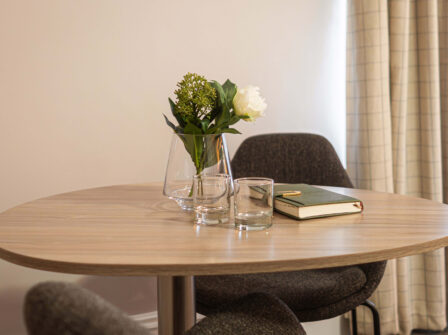 Elegant hotel room table with a vase of flowers, two water glasses, and a book inviting relaxation.