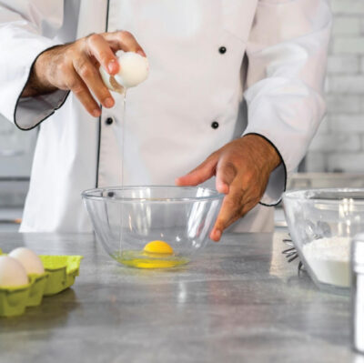 Chef cracks egg in modern hotel kitchen, showcasing dining experience.