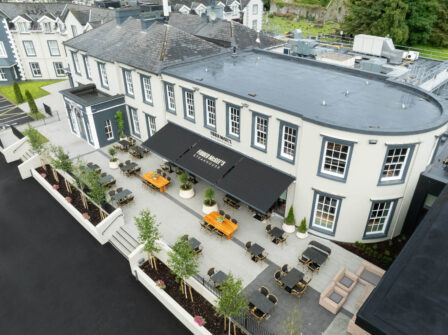 Aerial view of elegant historic hotel with outdoor dining area, stylish seating, and lush greenery, inviting guests to relax.