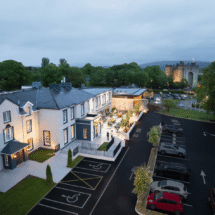Aerial view of charming hotel with outdoor seating, lush greenery, and nearby castle; convenient parking and accessible pathways.