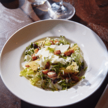 Delicious Caesar salad with croutons and bacon in elegant hotel dining, paired with wine on a wooden table.