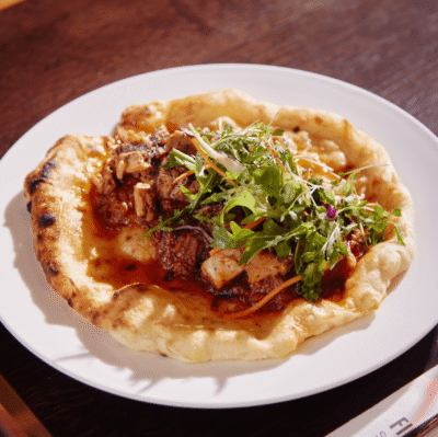 Succulent grilled chicken on flatbread with fresh rocket served in cosy hotel dining area, perfect for food lovers.