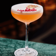 Luxurious cocktail with frothy top, garnished with dried citrus and red sprinkles on a marble bar at elegant hotel lounge.