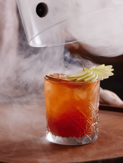 Elegant cocktail with apple garnish and smoke, showcasing luxurious hotel bar experience.