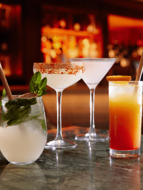 Elegant hotel bar with a variety of colourful cocktails, including mojitos and margaritas, on a marble counter under warm lighting.