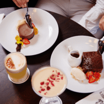 Guests enjoying elegant desserts and cocktails at a stylish hotel restaurant table, featuring fresh fruit garnishes.