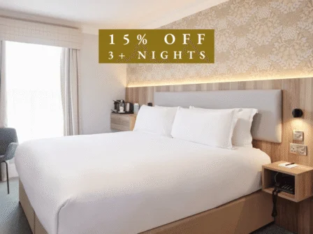 Elegant hotel room with plush double bed, floral wallpaper, and a coffee station, offering a warm and inviting stay.
