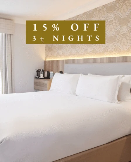 Elegant hotel room with plush double bed, floral wallpaper, and a coffee station, offering a warm and inviting stay.