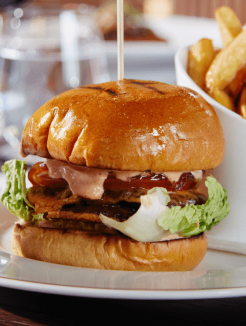 Gourmet burger with fresh lettuce and crispy chips on elegant dining setup at hotel restaurant.