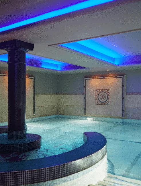 Luxurious indoor pool with ambient blue lighting and elegant mosaic decor at hotel spa. Perfect for relaxation and rejuvenation.