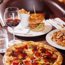 Enjoy gourmet dining with pepperoni pizza, gourmet burger, and red wine in a cosy hotel restaurant setting.