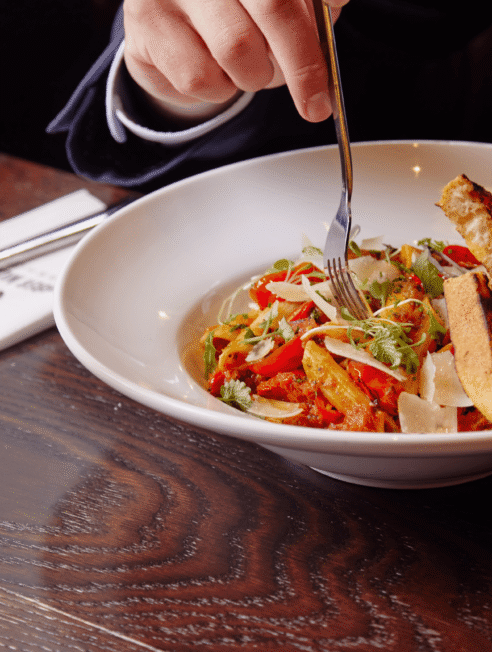 Guest enjoying a gourmet pasta dish with grilled bread in elegant hotel restaurant, paired with a glass of white wine.