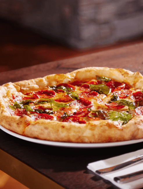 Savour a delicious gourmet pizza with fresh basil and pepperoni in the hotel's elegant restaurant setting.