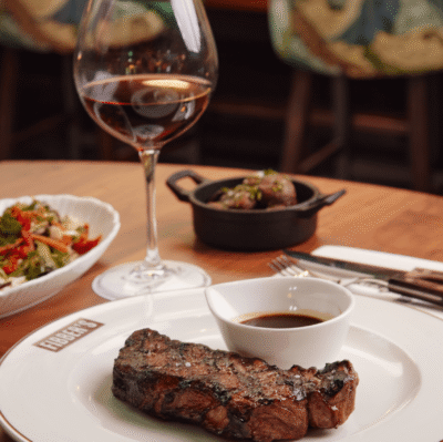 Savour succulent steak with rich sauce, paired with fine wine, in stylish hotel restaurant offering exquisite dining experience.