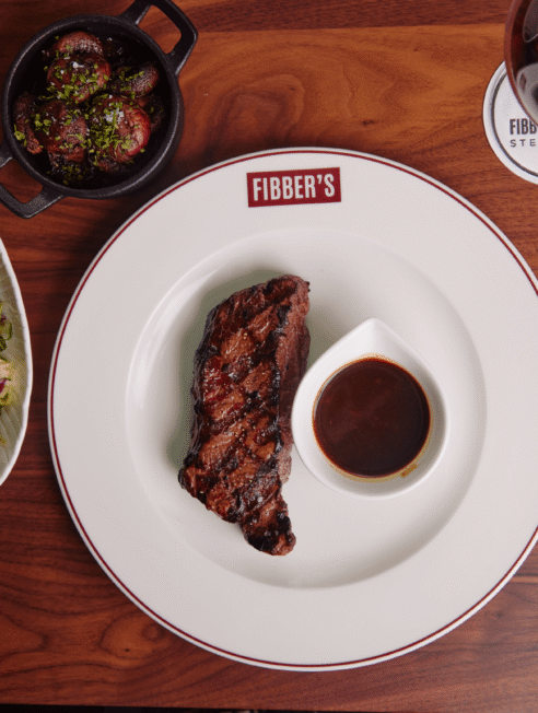 Savour succulent steak with rich sauce, fresh salad, and fine wine at Fibber's Steakhouse for a refined dining experience.